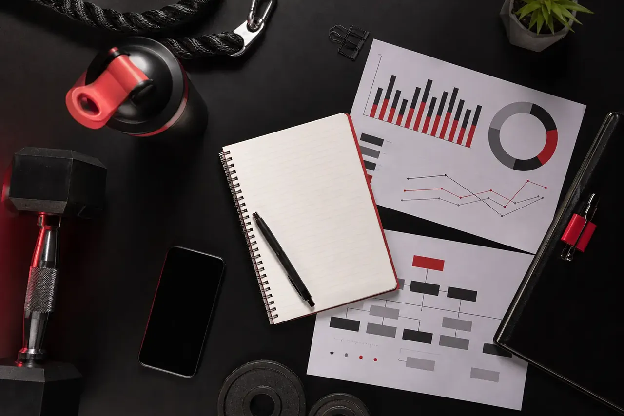 Grafici di fatturato e KPI su una scrivania accanto ad attrezzi da palestra