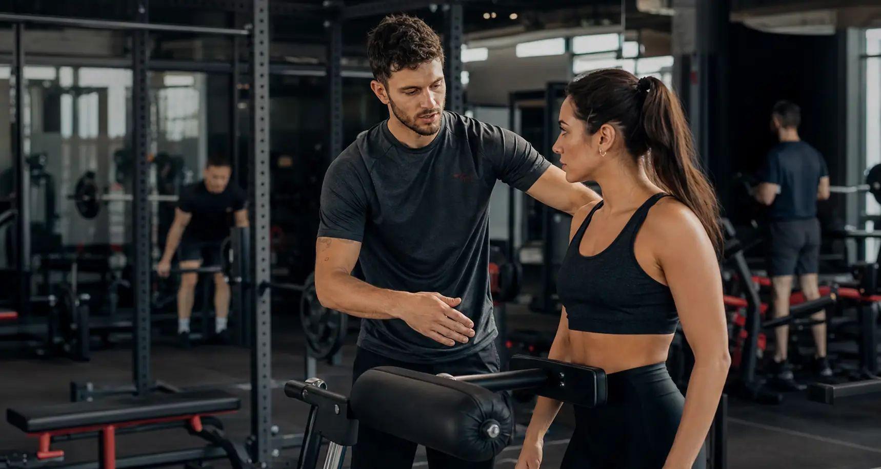 Personal trainer che applica il metodo in palestra con una cliente davanti a un macchinario